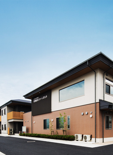 介護施設の建物外観。黒と白のモダンデザイン、茶色のレンガ調壁面が特徴